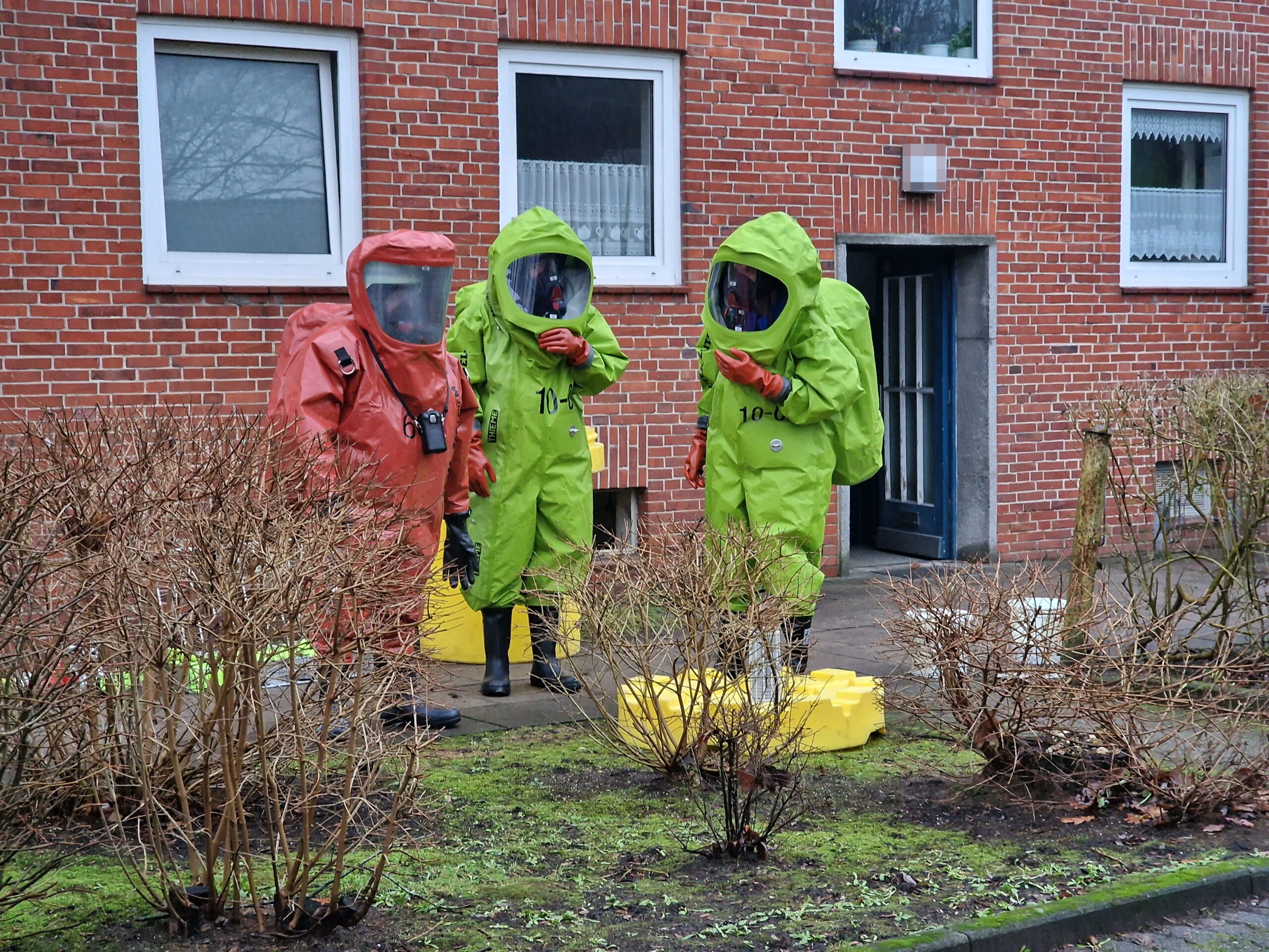 Zu sehen sind drei Feuerwehrleute in Schutzanzügen vor dem Wohnhaus in Rendsburg