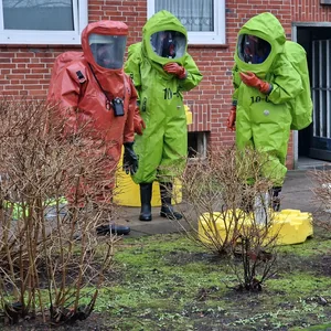 Zu sehen sind drei Feuerwehrleute in Schutzanzügen vor dem Wohnhaus in Rendsburg