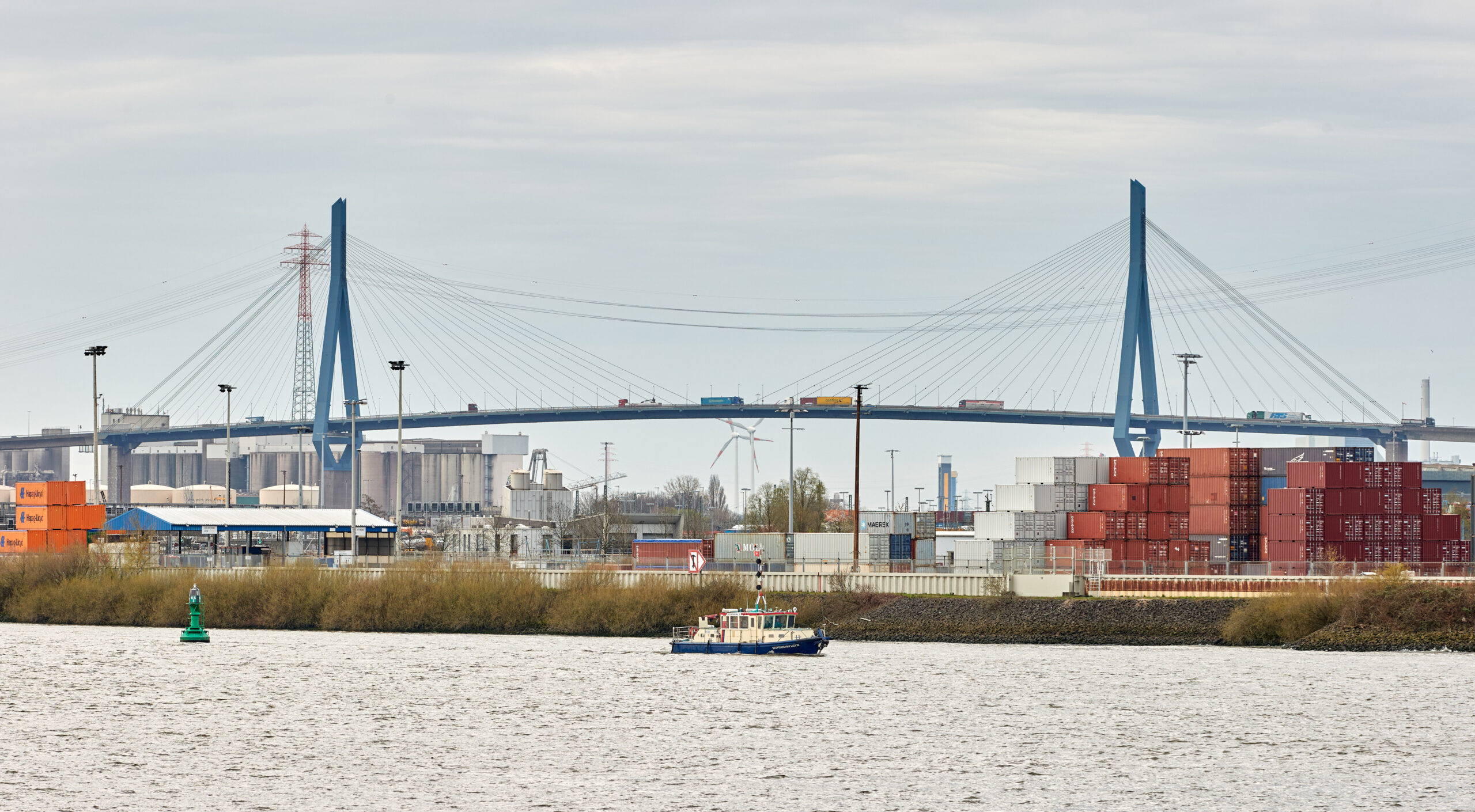 Lastwagen fahren über die Köhlbrandbrücke. Auf der Elbe fährt ein Schiff. Im Hintergrund sind Container zu sehen.