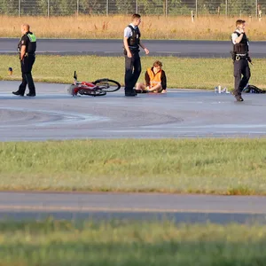 Klimaaktivisten kleben auf einem Rollfeld des Hamburger Flughafens. Daneben stehen zwei Polizeiautos und Polizeibeamte. (Archivbild)