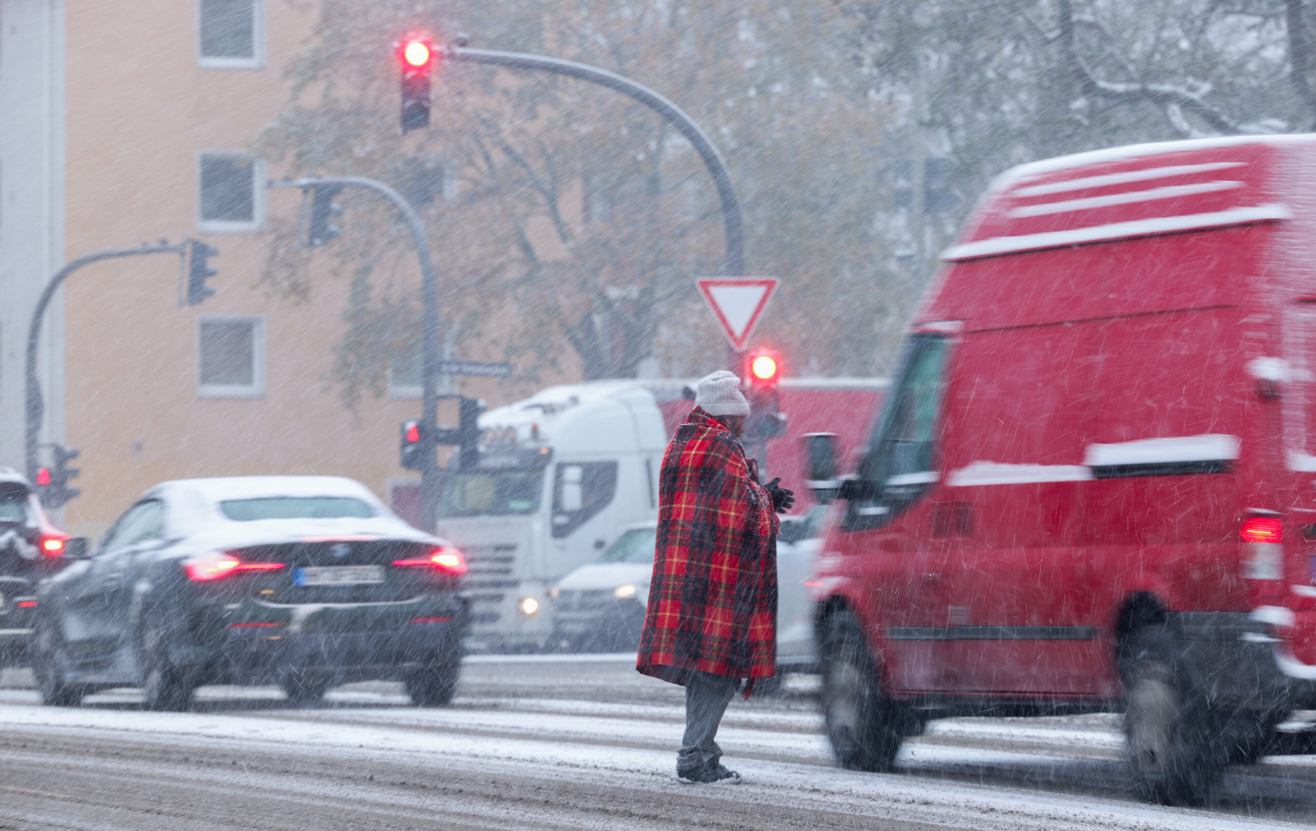 Ein Mann steht im Schneetreiben auf einer Hamburger Kreuzung und bittet um Almosen.