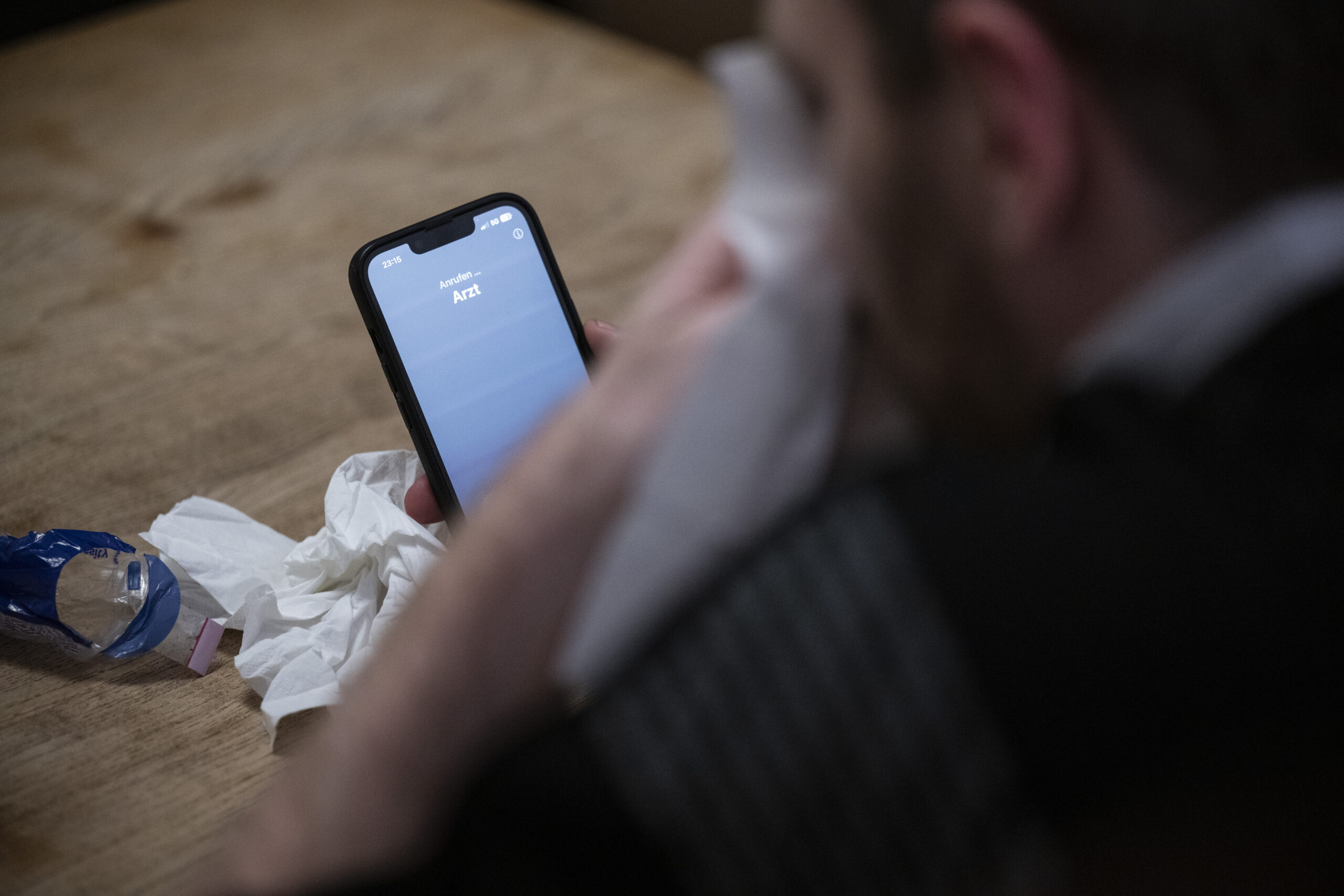 Ein Mann hält ein Taschentuch in einer Hand und ruft mit seinem Smartphone beim Arzt an. (Symbolbild)