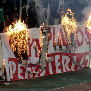 Brennende Plakate am Spielfeldrand, davor eine vermummte Person