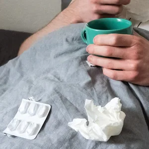 Ein Mann liegt mit Taschentüchern, Teetasse, Nasenspray und Tabletten im Bett. (Symbolbild)