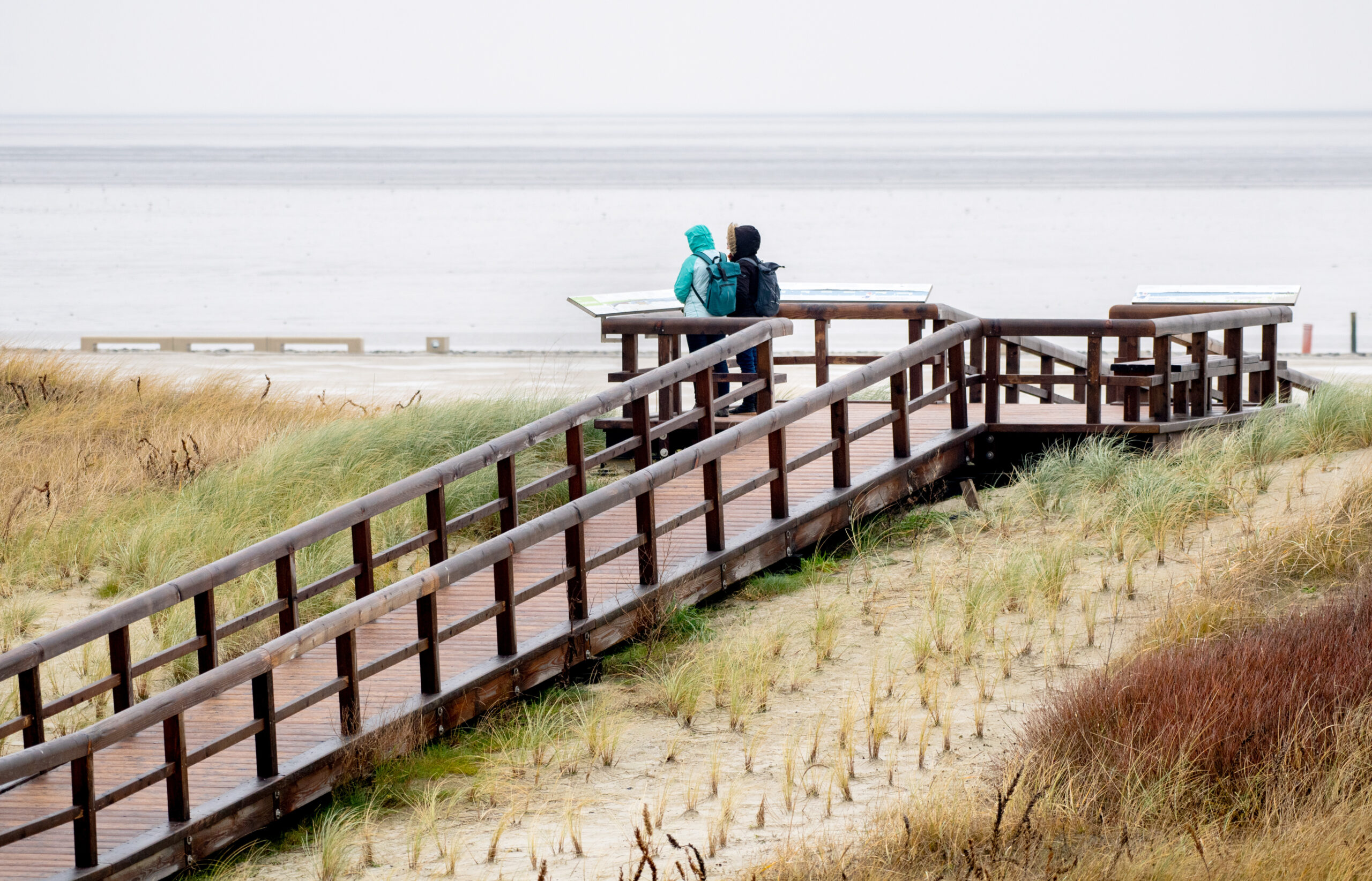 Zwei Frauen stehen bei regnerischem Wetter auf einer Aussichtsplattform am Strand und schauen auf die Nordsee. (Symbolbild)