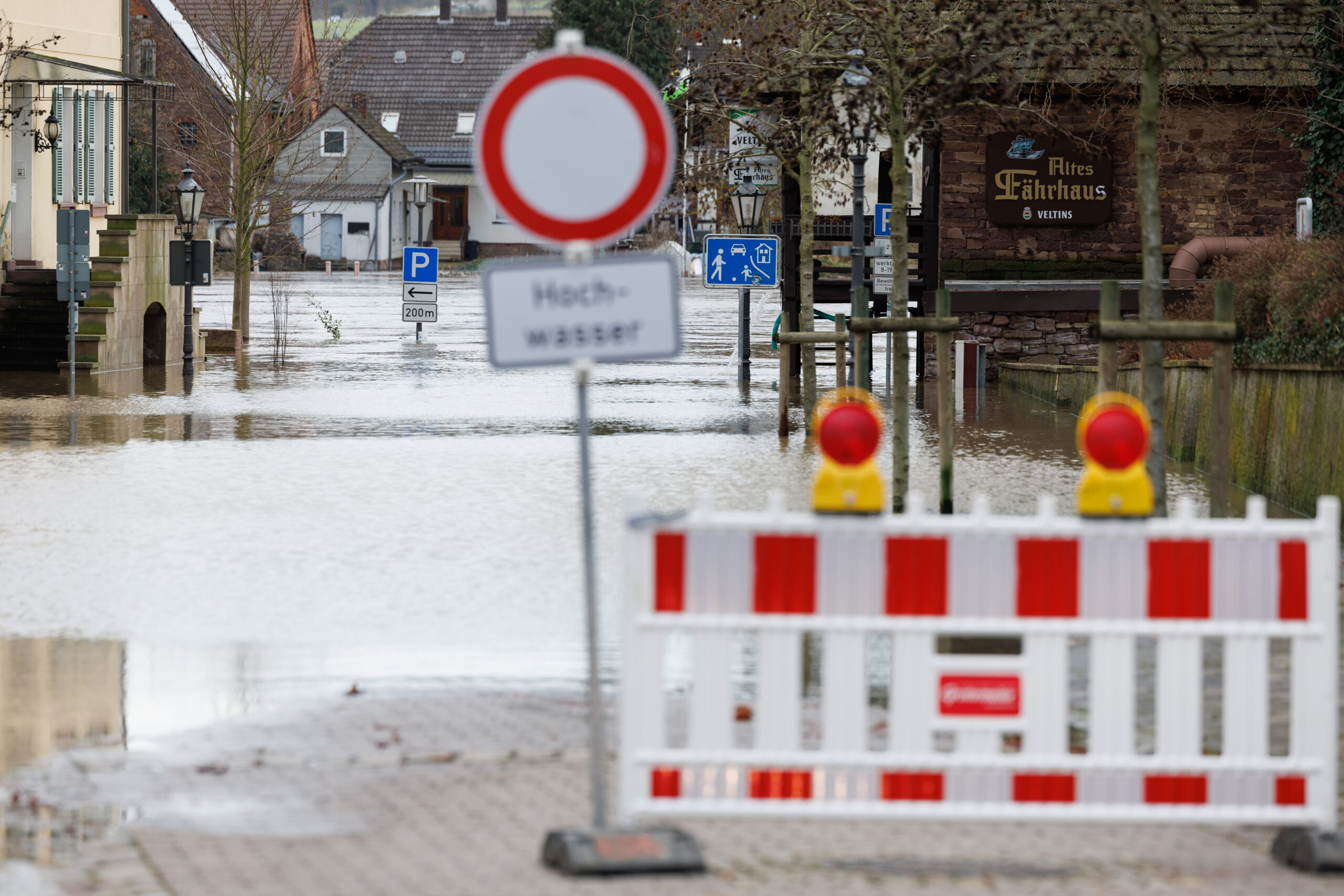 Blick auf eine überflutete Straße hinter einer Straßensperrung mit dem Hinweis „Hochwasser“