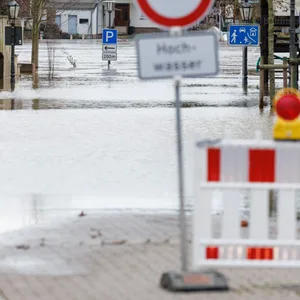 Blick auf eine überflutete Straße hinter einer Straßensperrung mit dem Hinweis „Hochwasser“