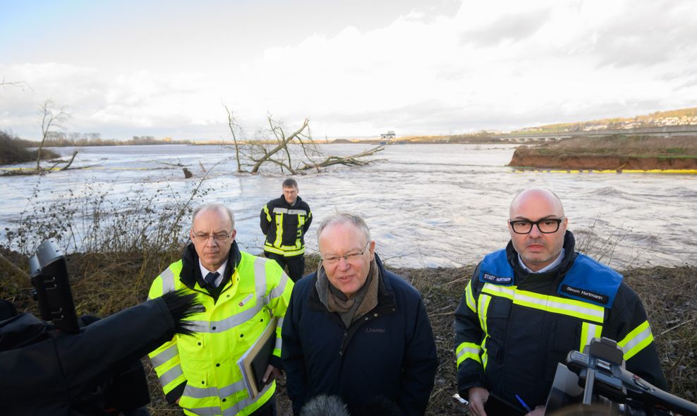 Stephan Weil (M, SPD), Ministerpräsident Niedersachsen, Dieter Rohrberg (l), Landesbranddirektor Niedersachsen, und Simon Hartmann, Bürgermeister Northeim, stehen vor einem gebrochenen Damm an der Ruhme bei Northeim.