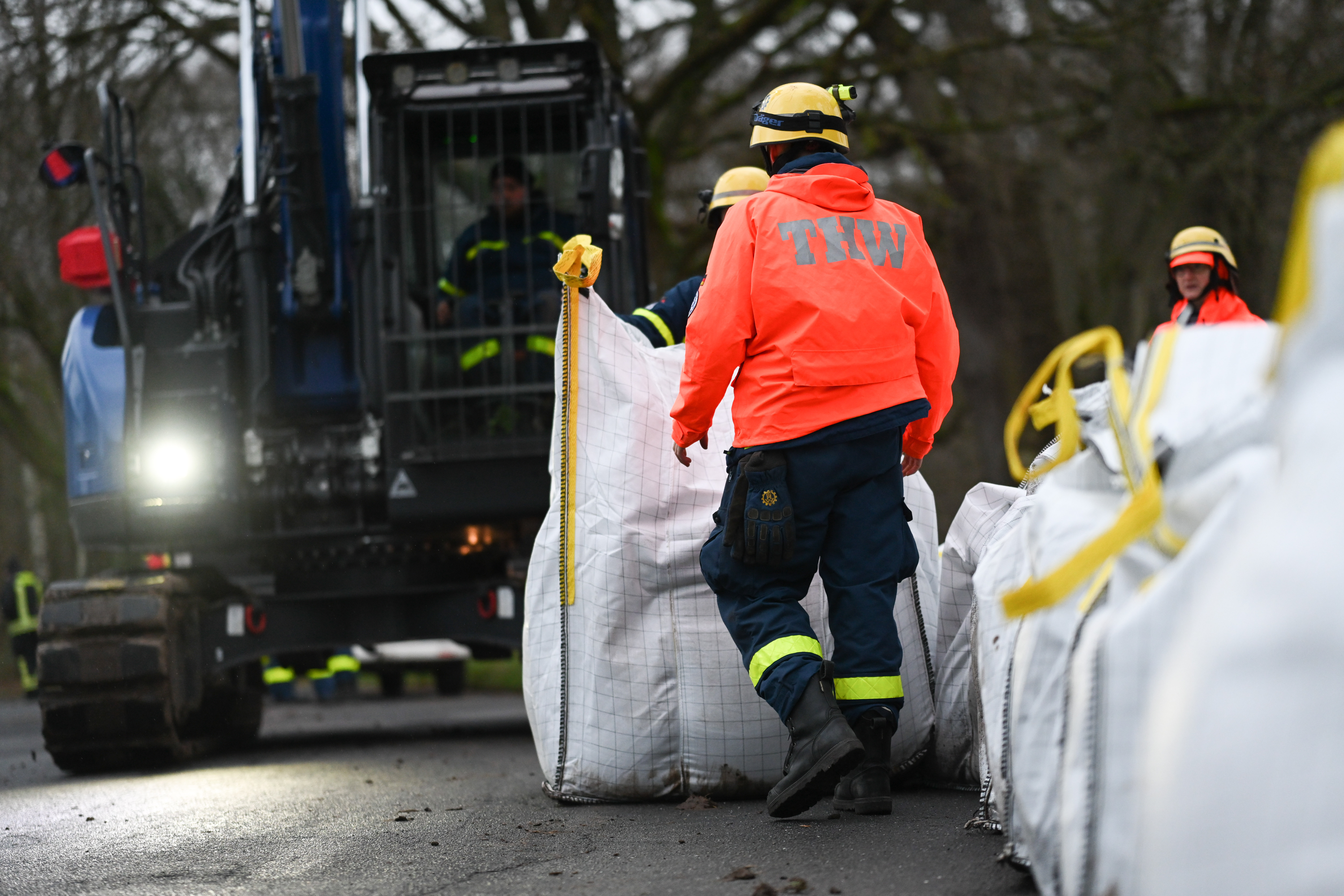 Ehrenamtliche Einsatzkräfte der Feuerwehr und des Technischen Hilfswerks (THW) bauen einen Mobildeich mit Sandsäcken auf, um ein Wohngebiet unweit der Ems zu sichern.