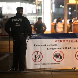 Polizeibeamte stehen an der Böllerverbotszone am Alexanderplatz an einem Hinweisschild.