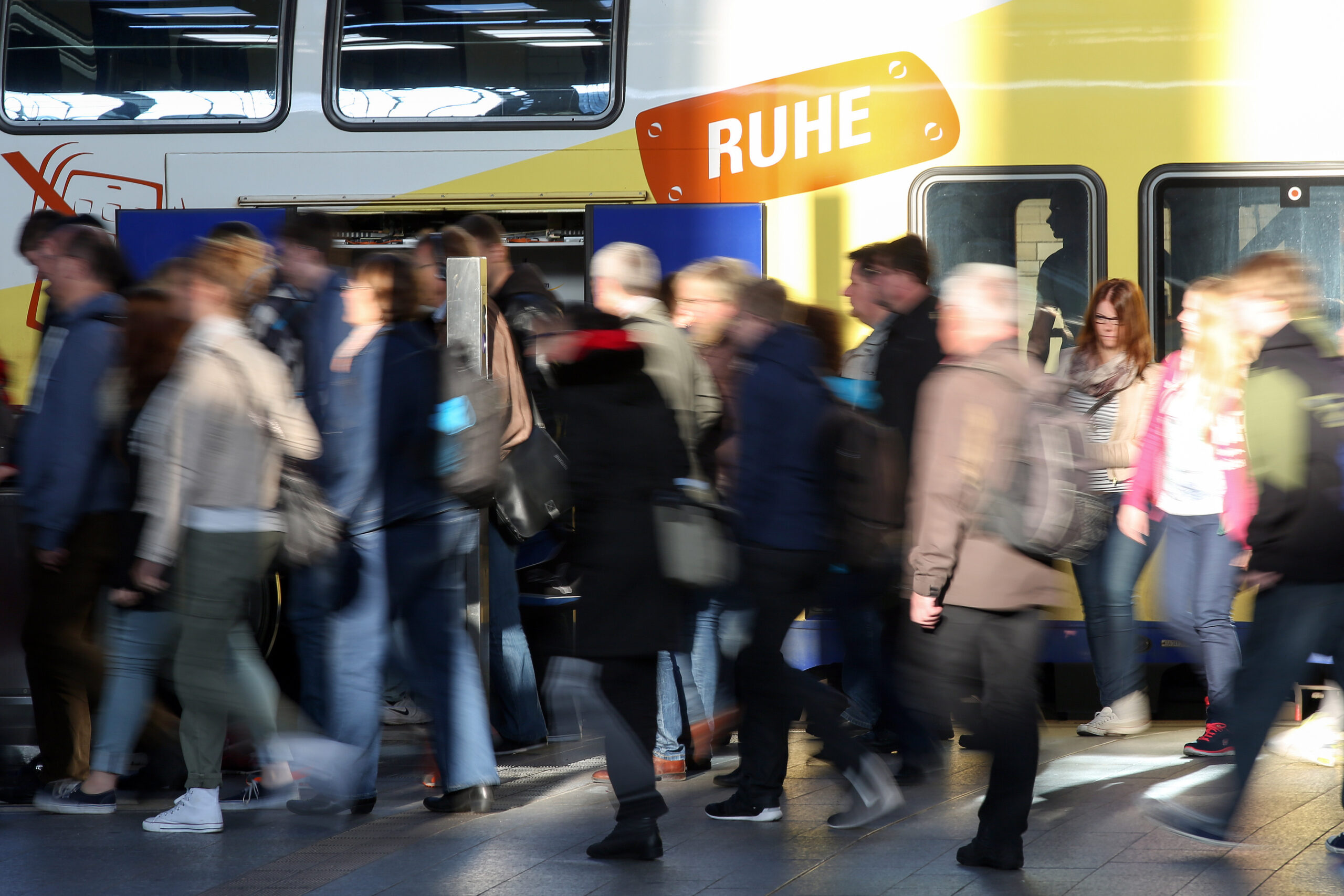 Reisende und Pendler laufen auf einem Bahnsteig an einem stehenden Metronom-Zug vorbei.