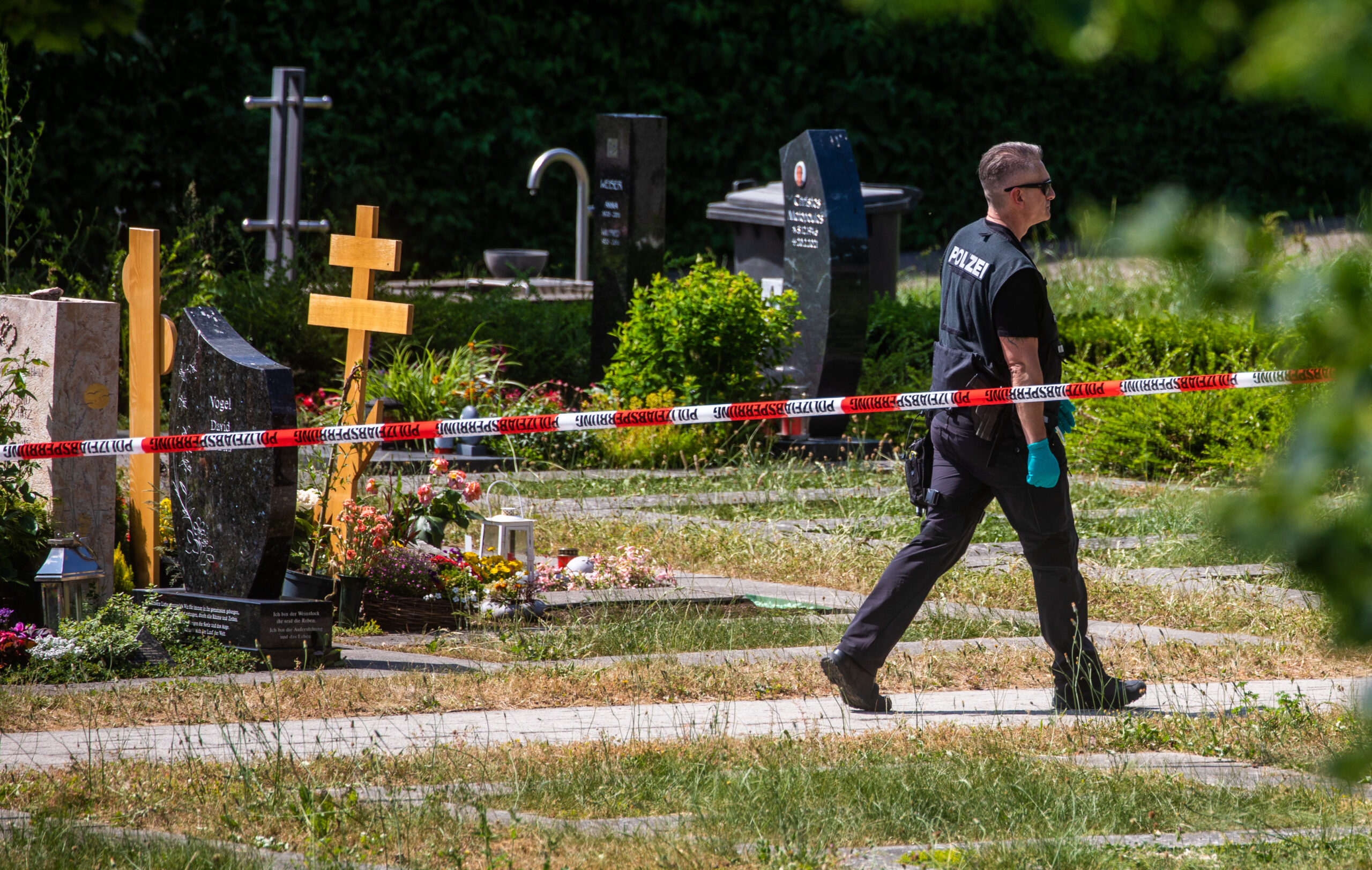 Ein Polizist geht über den abgesperrten Teil des Tatorts auf einem Friedhof.