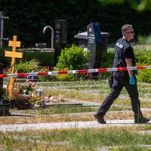 Ein Polizist geht über den abgesperrten Teil des Tatorts auf einem Friedhof.