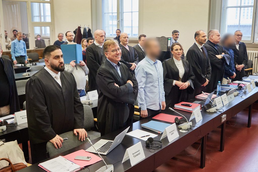 Die Angeklagten und ihre Anwälte stehen im Gerichtssaal.