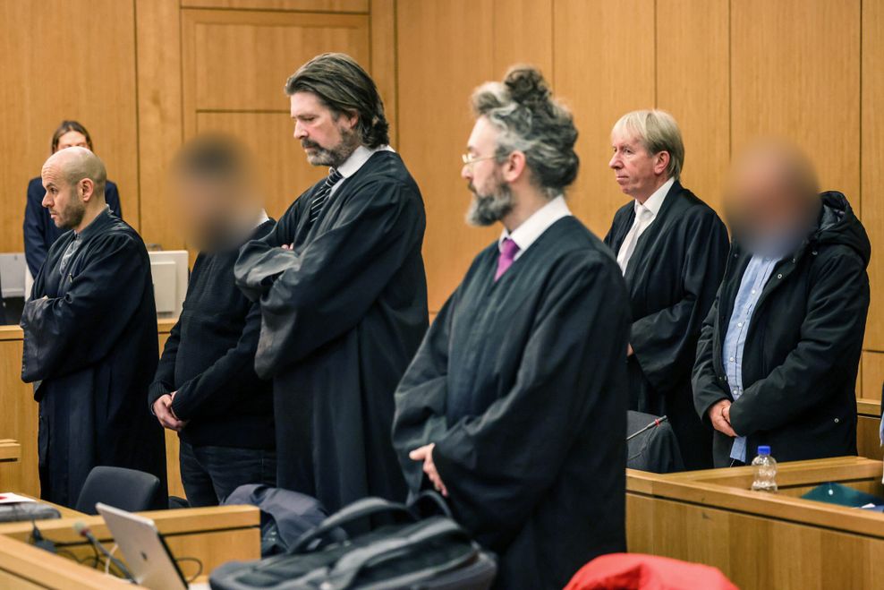 Die Angeklagten (2.v.l. und r.) stehen zwischen ihren Anwälten im Gerichtssaal.
