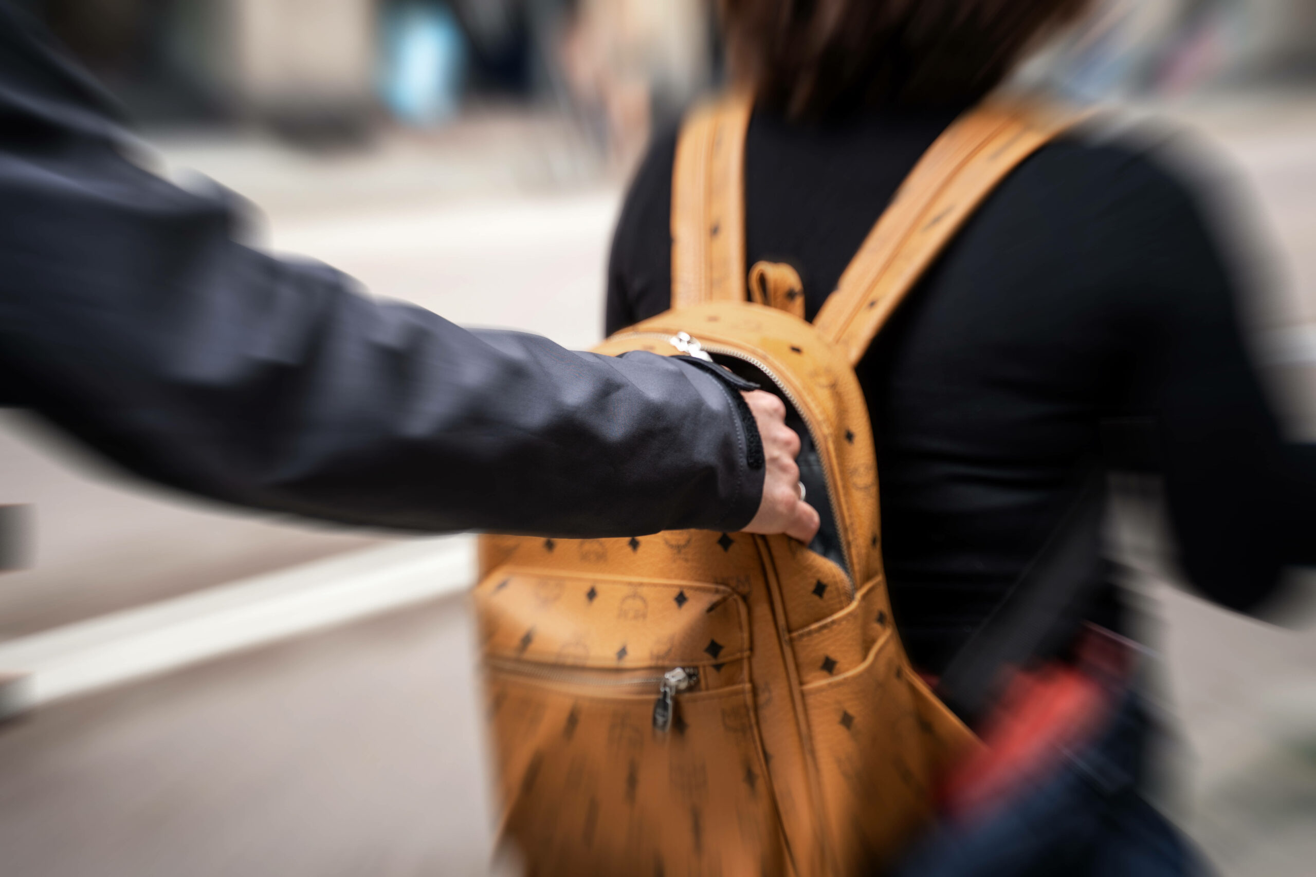 Symbolbild eines Taschendiebstahls: Einer Person wird von hinten in den Rucksack gegriffen