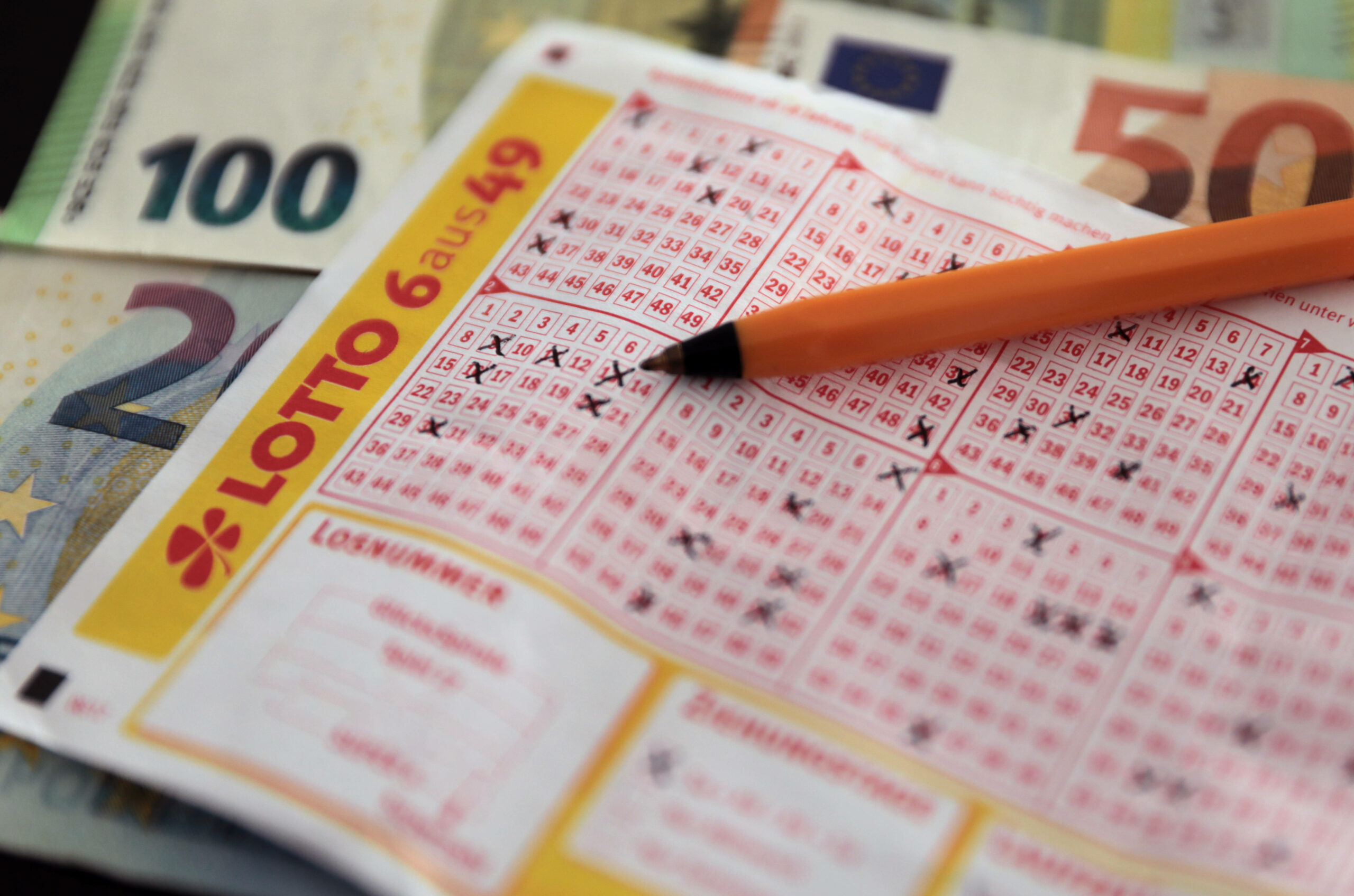 Ein ausgefüllter Lottoschein, ein Stift und Geldscheine liegen auf einem Tisch. (Symbolbild)
