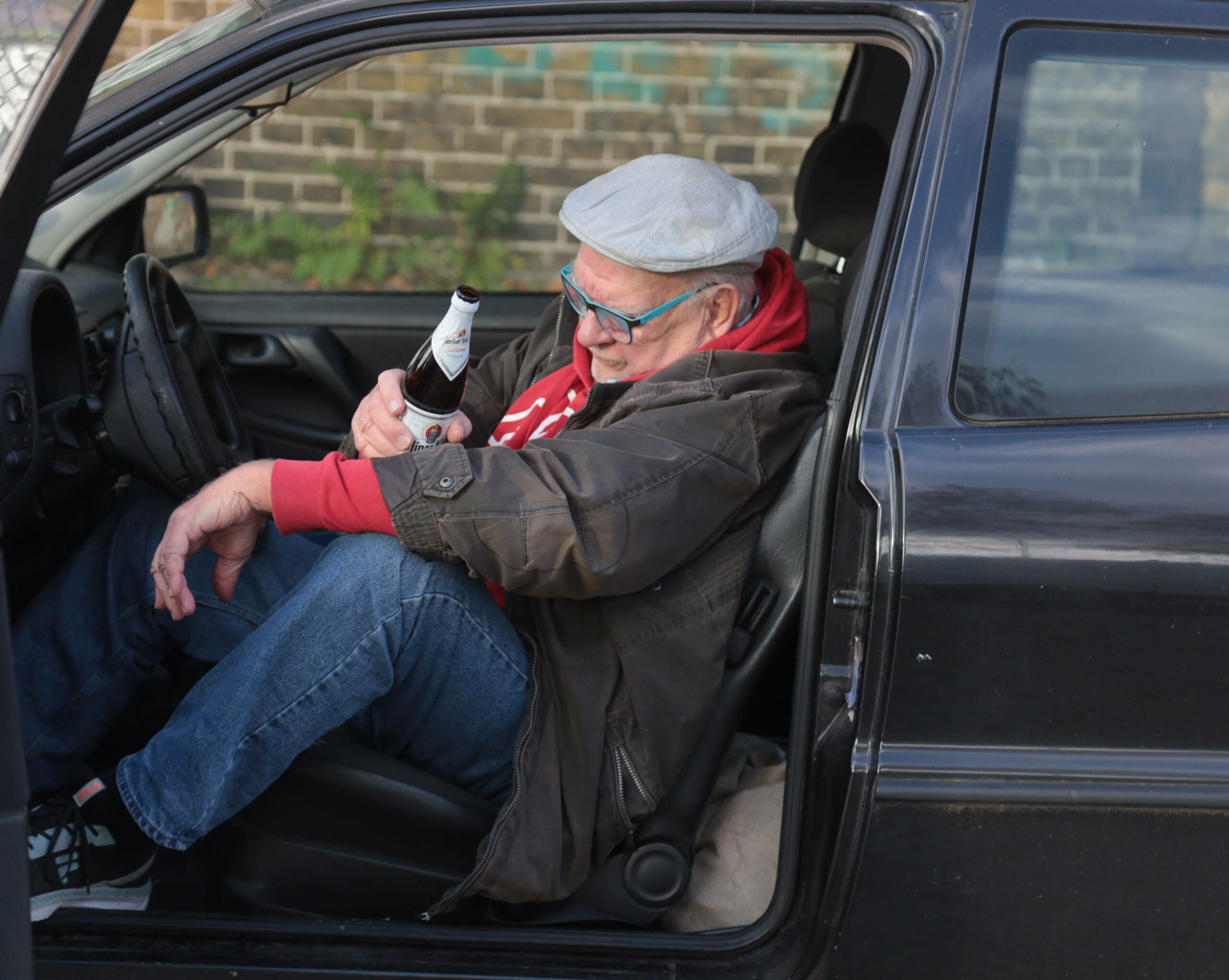 Ein Mann sitzt mit einer Bierflasche in der Hand im Auto. (Symbolbild)