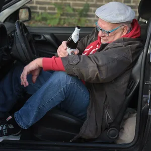 Ein Mann sitzt mit einer Bierflasche in der Hand im Auto. (Symbolbild)