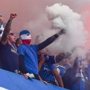 Hansa Rostock-Hooligans stehen vemummt auf der Tribüne und zünden Pyros