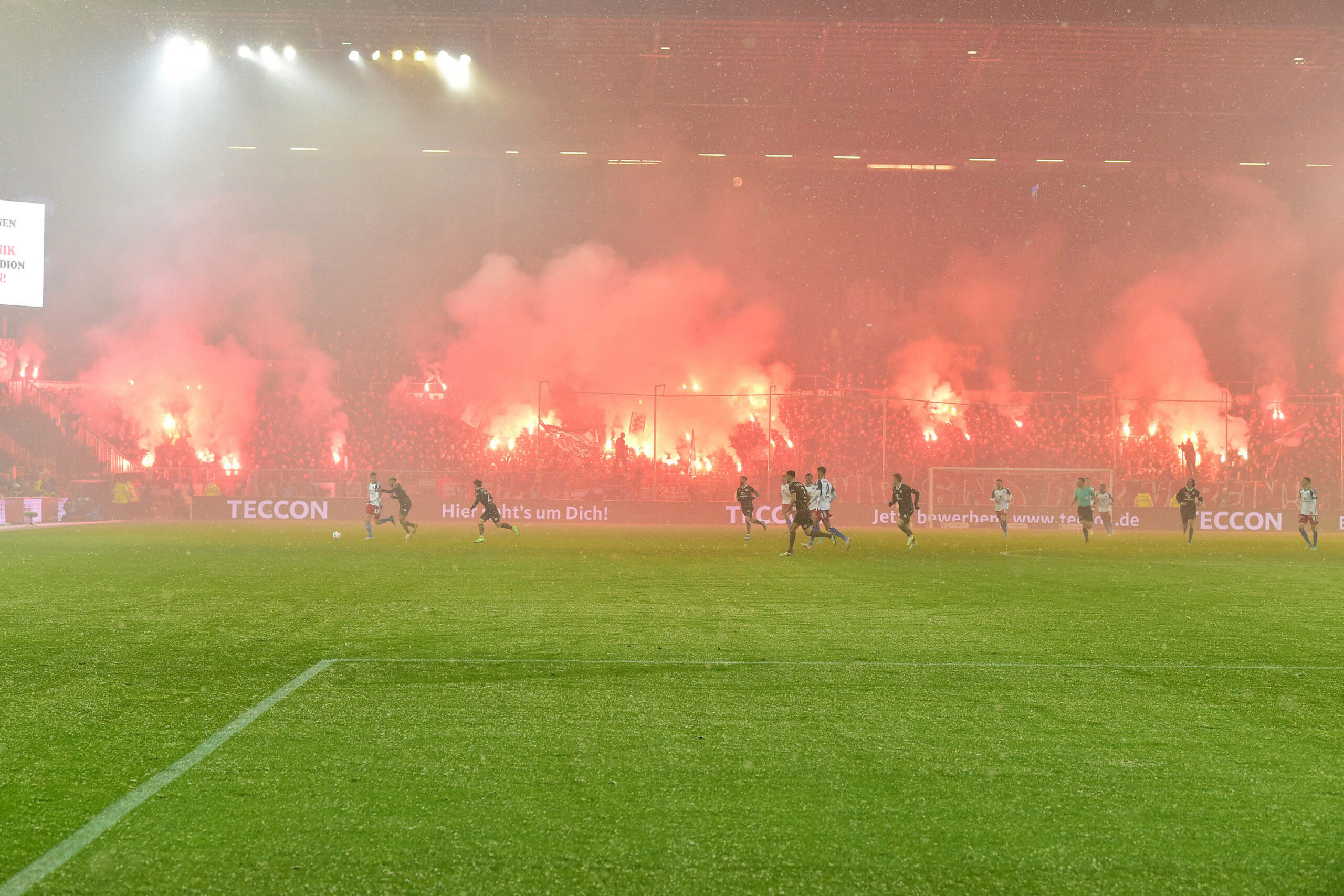 Im Hintergrund zünden die St. Pauli-Fans Bengalos, davor läuft das Spiel.