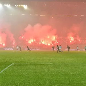 Im Hintergrund zünden die St. Pauli-Fans Bengalos, davor läuft das Spiel.