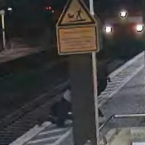 Oben rechts ist die heranfahrende Lok zu sehen. Vorne sieht man, wie der Mann in letzter Sekunde aus dem Gleisbereich gezogen wird