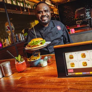 Bei „Burgerlich“, hier am Gänsemarkt, wird das Essen per iPad bestellt. Mitarbeiter Yawo Tenge (56) serviert den Burger.