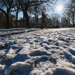 Schnee liegt im Stadtpark, eine Frau joggt auf dem Weg.