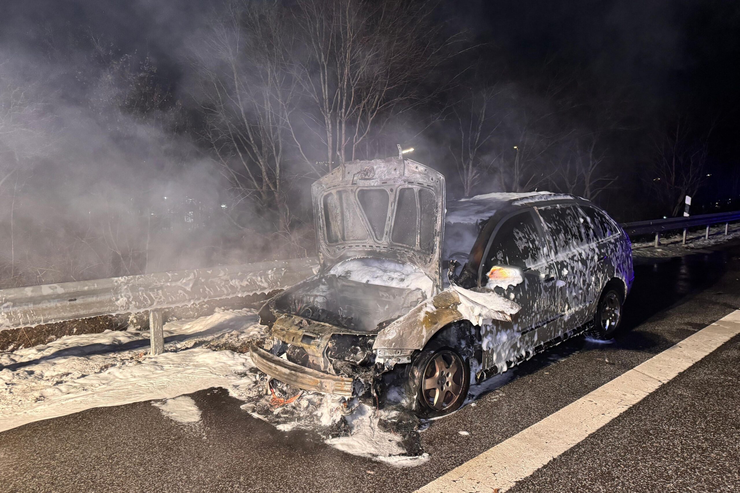 Der Skoda steht am Straßenrand, Front und Motorrad sind verbrannt, das Auto ist mit Löschschaum bedeckt.