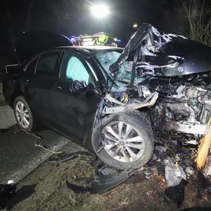 Ein schwarzer Mercedes ist gegen einen Baum geknallt, die Motorhaube ist völlig verbeult.