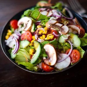 Eine Schüssel mit Salat aus Gurken, Mais, Zwiebeln, Tomaten und anderem Gemüse steht auf einem Tisch.