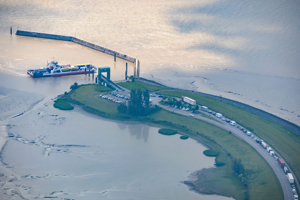 Eine Fähre der Reederei FRS Elbfähre fährt auf der Elbe vor dem Glückstädter Anleger der Fähre Glückstadt-Wischhafen während auf der B495 zahlreiche Fahrzeuge und Lastwagen warten. (Archivbild)