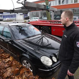 Ein Behördenmitarbeiter steht vor einem Mercedes, der gleich auf einen Abschleppwagen gehievt wird.