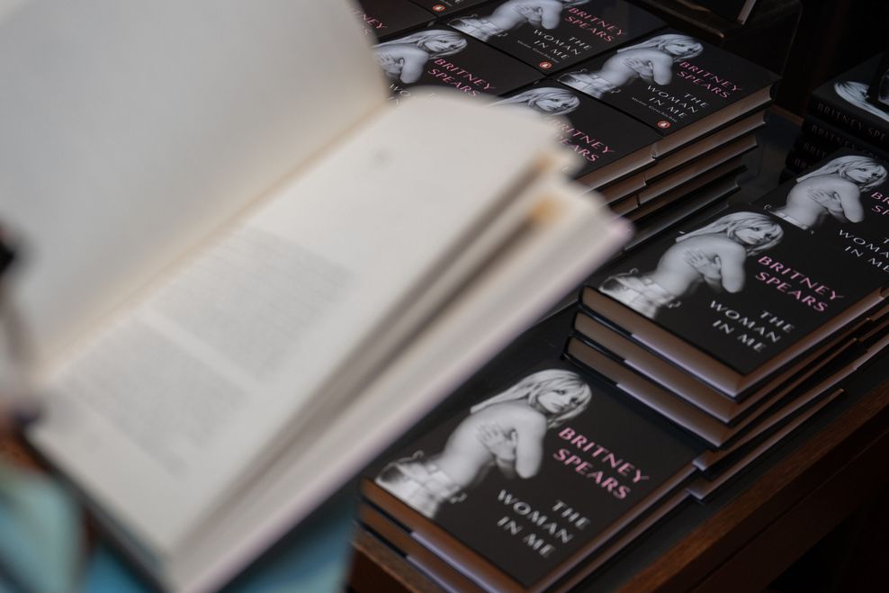 Eine Frau hält eine Ausgabe von „The Woman in Me“, der Autobiografie von Britney Spears, in der Hand.