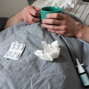 Mann mit Taschentüchern und Tee im Bett