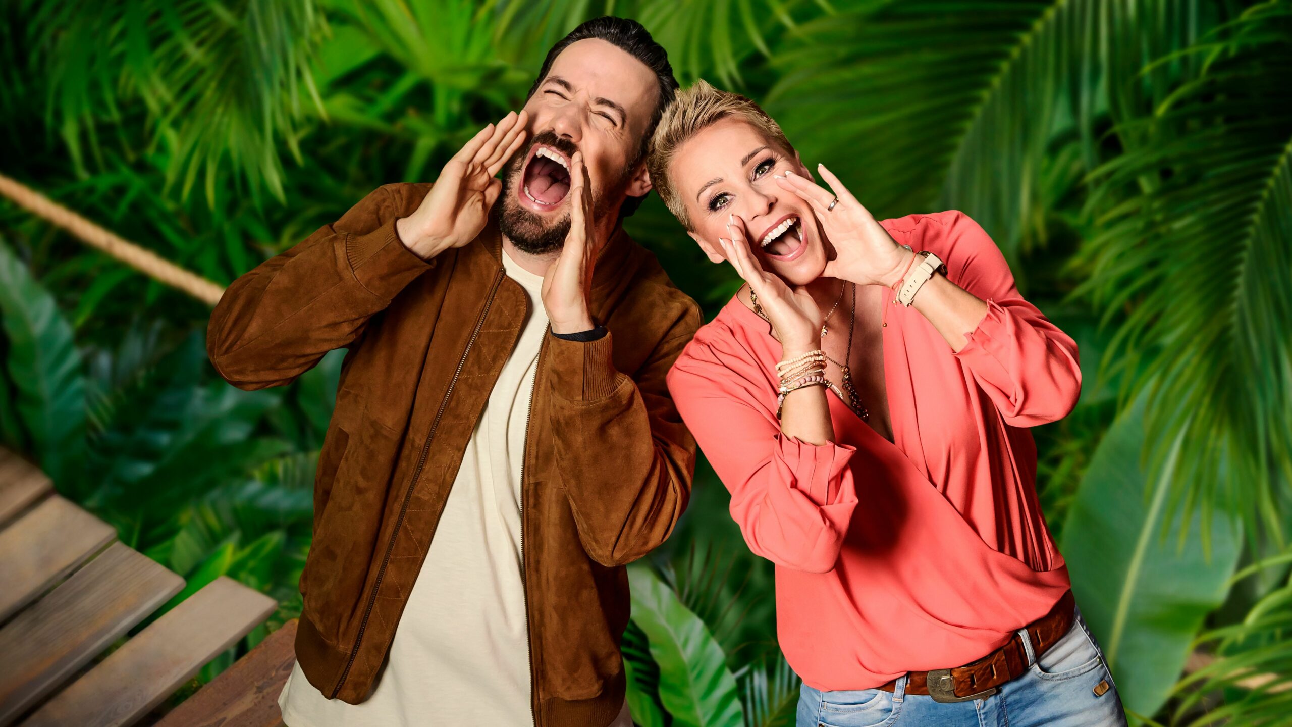 Die Moderatoren Jan Köppen und Sonja Zietlow vom RTL-Dschungelcamp „Ich bin ein Star – Holt mich hier raus!“ stehen in einer Dschungel-Kulisse.