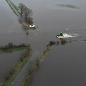 Ein Traktor fährt über eine überflutete Straße im Hochwassergebiet im Emsland.