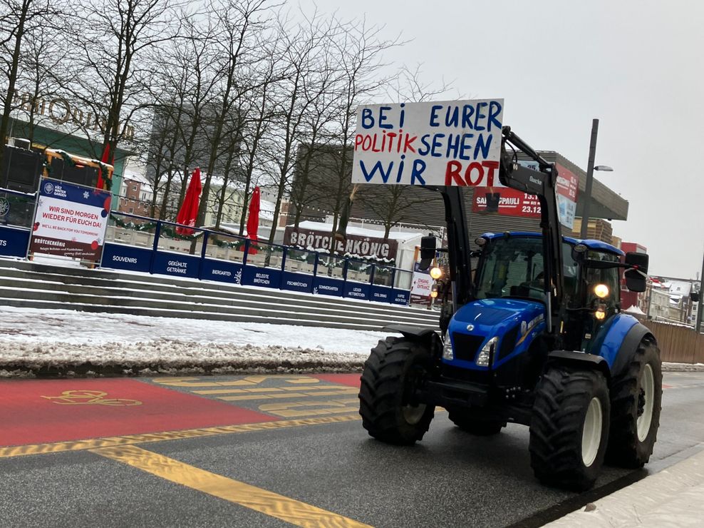 An einem Traktor ist ein Schild mit der Aufschrift „Bei eurer Politik sehen wir Rot“ zu sehen.