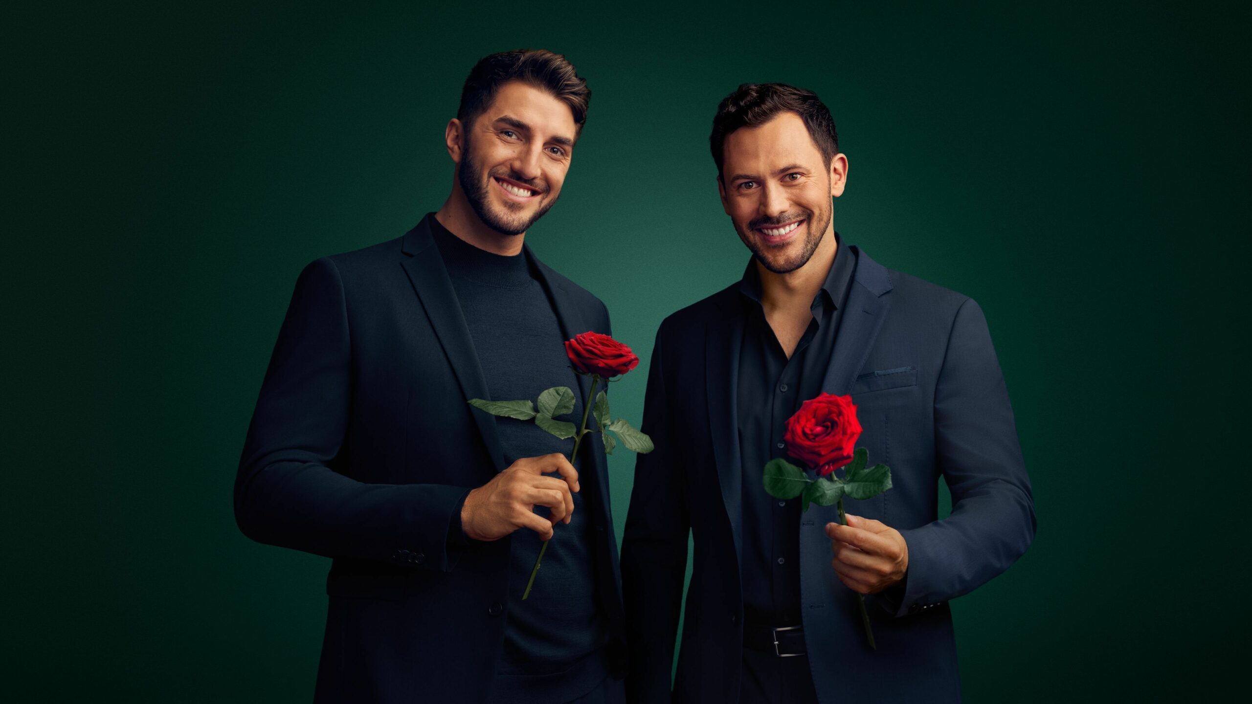 Dennis (l.) und Sebastian (r.), die Teilnehmer der RTL-Kuppelshow „Die Bachelors“. Sie lachen und halten jeweils eine rote Rose in einer Hand.
