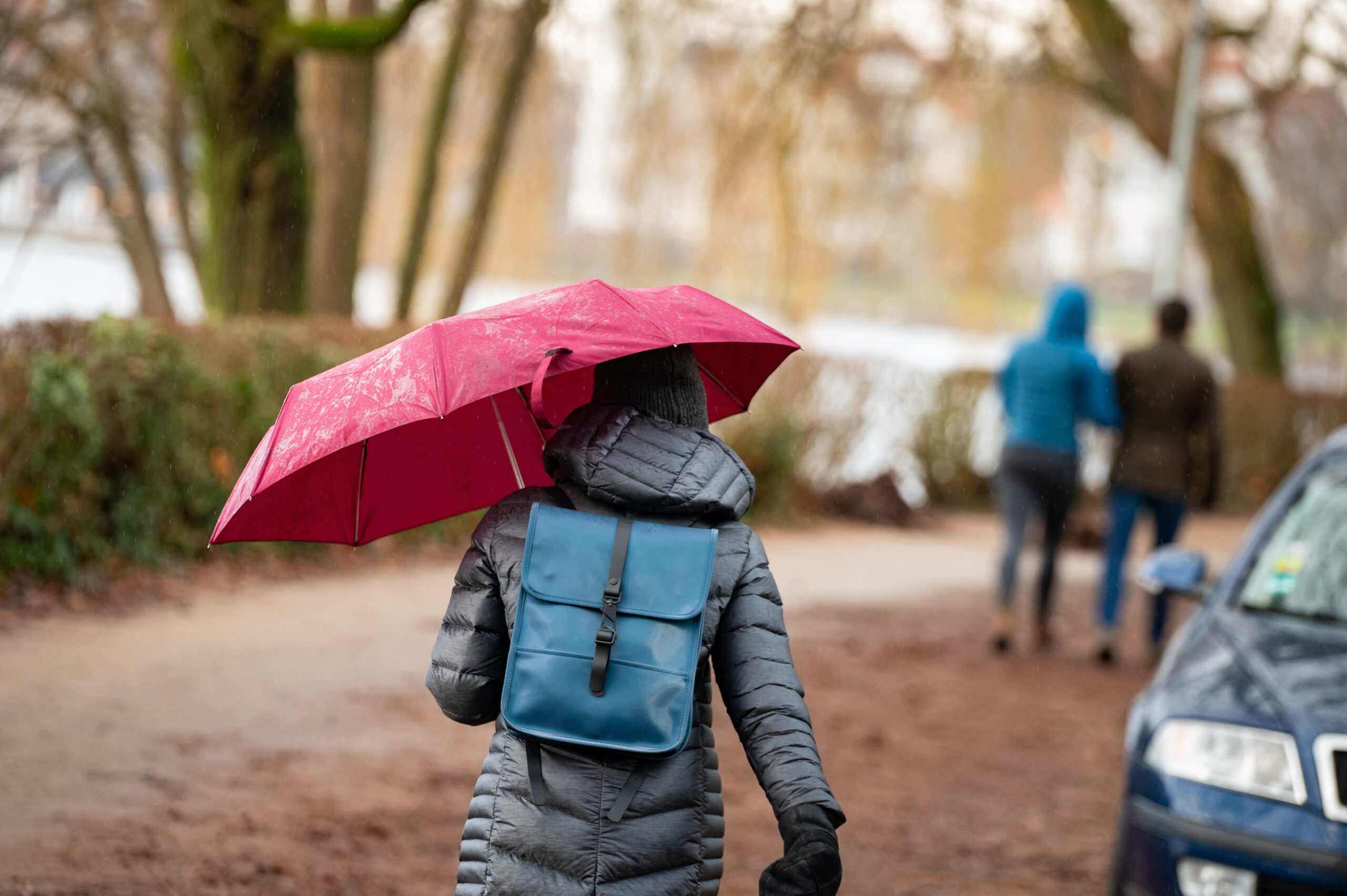 Eine Spaziergängerin ist mit einem roten Regenschirm unterwegs.