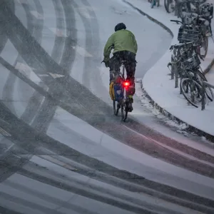 Ein Fahrradfahrer fährt am Morgen eine verschneite Straße entlang.