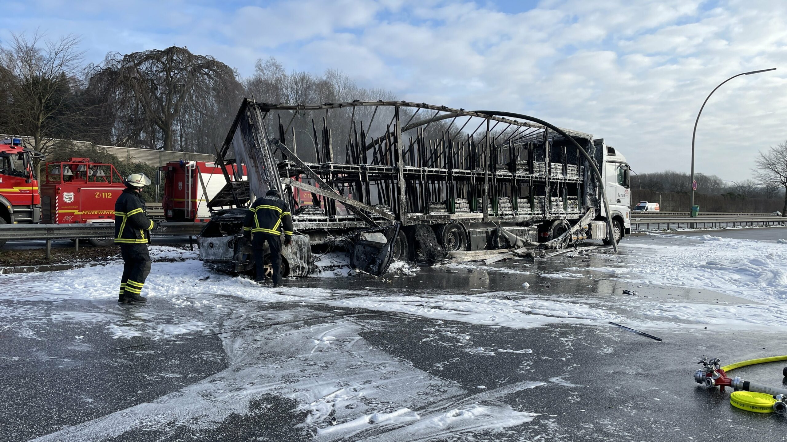 Feuerwehrleute stehen an einem ausgebrannten Lastwagen