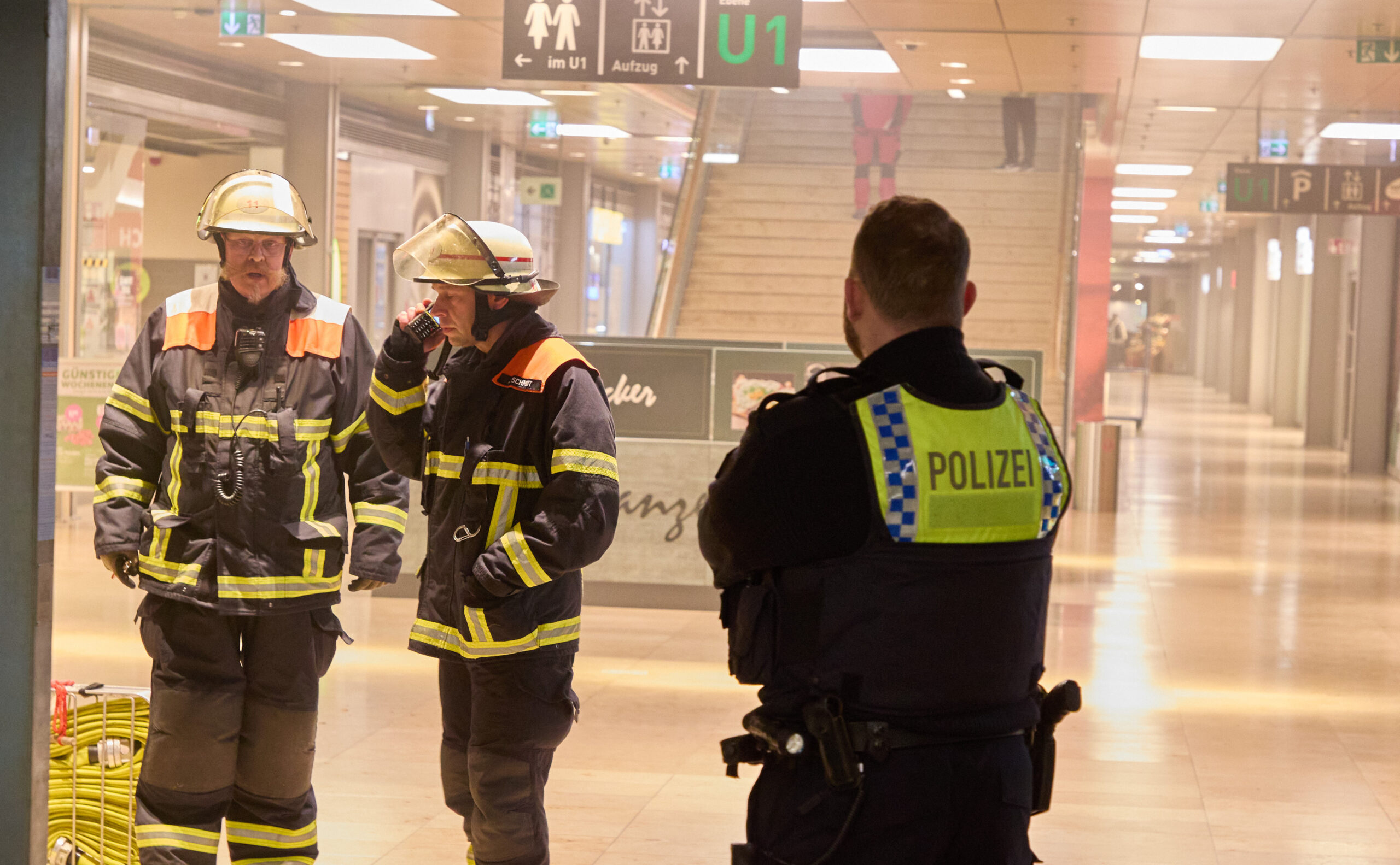 Ein Polizist und zwei Männer der Feuerwehr stehen in der verrauchten Europa-Passage.