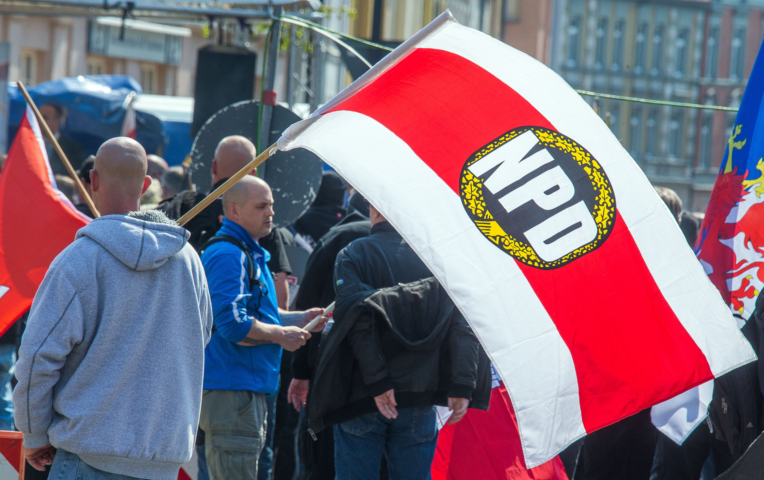 Teilnehmer einer Kundgebung der NPD in der Innenstadt von Schwerin halten Fahnen mit dem Parteilogo in der Hand. (Archivbild)
