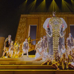 Bühne vom vorne fotografiert, das Ensemble steht und sitzt in Kostümen rund um einen mit Gold geschmückten Elefanten