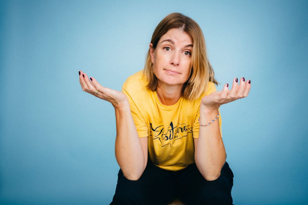 Frau sitzend und gestikulierend, Handhaltung und Gesichtsausdruck könnten als "tja" gelesen werden