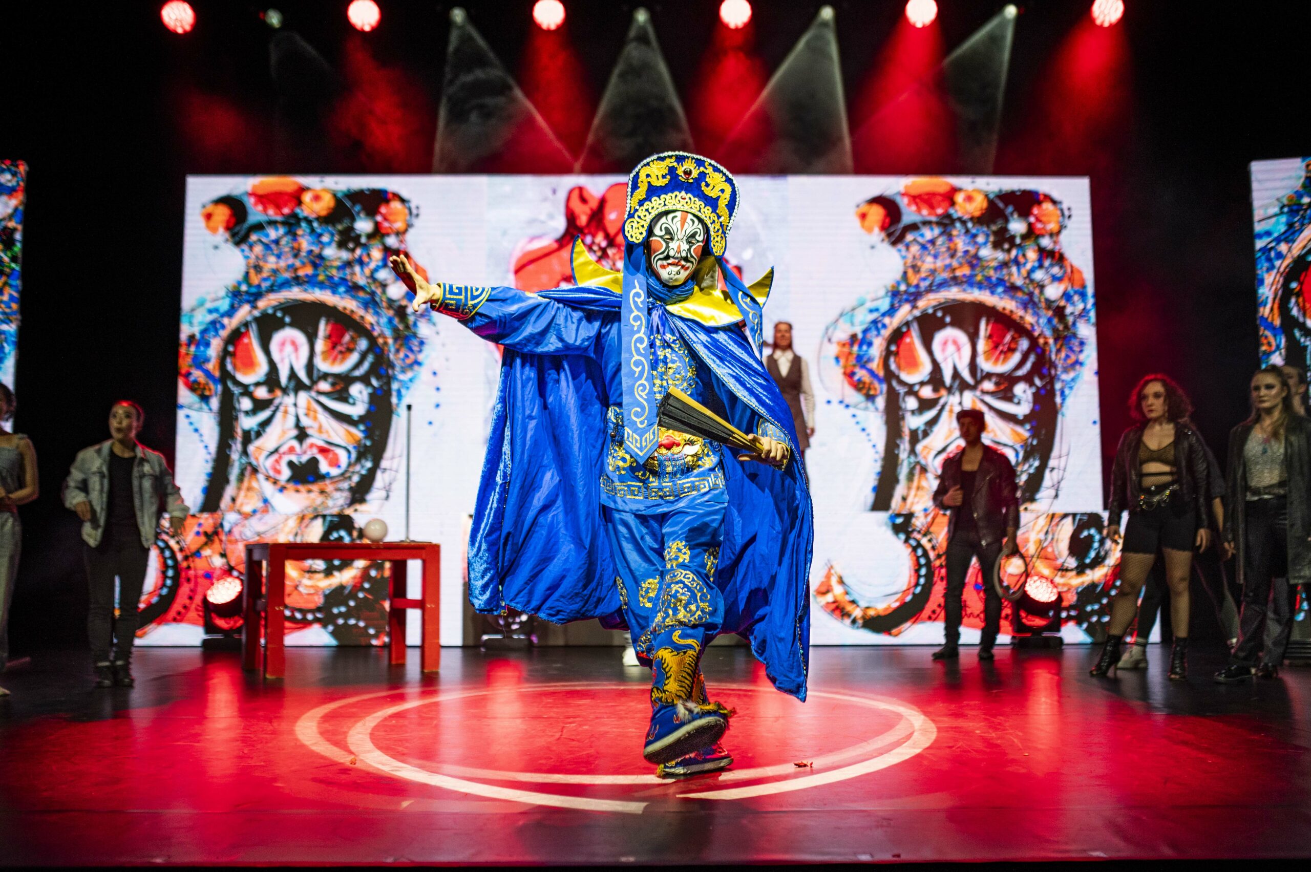 Tänzer in chinesischer Tracht, im Hintergrund auf der Bühne stehen Darstellerinnen und Darsteller