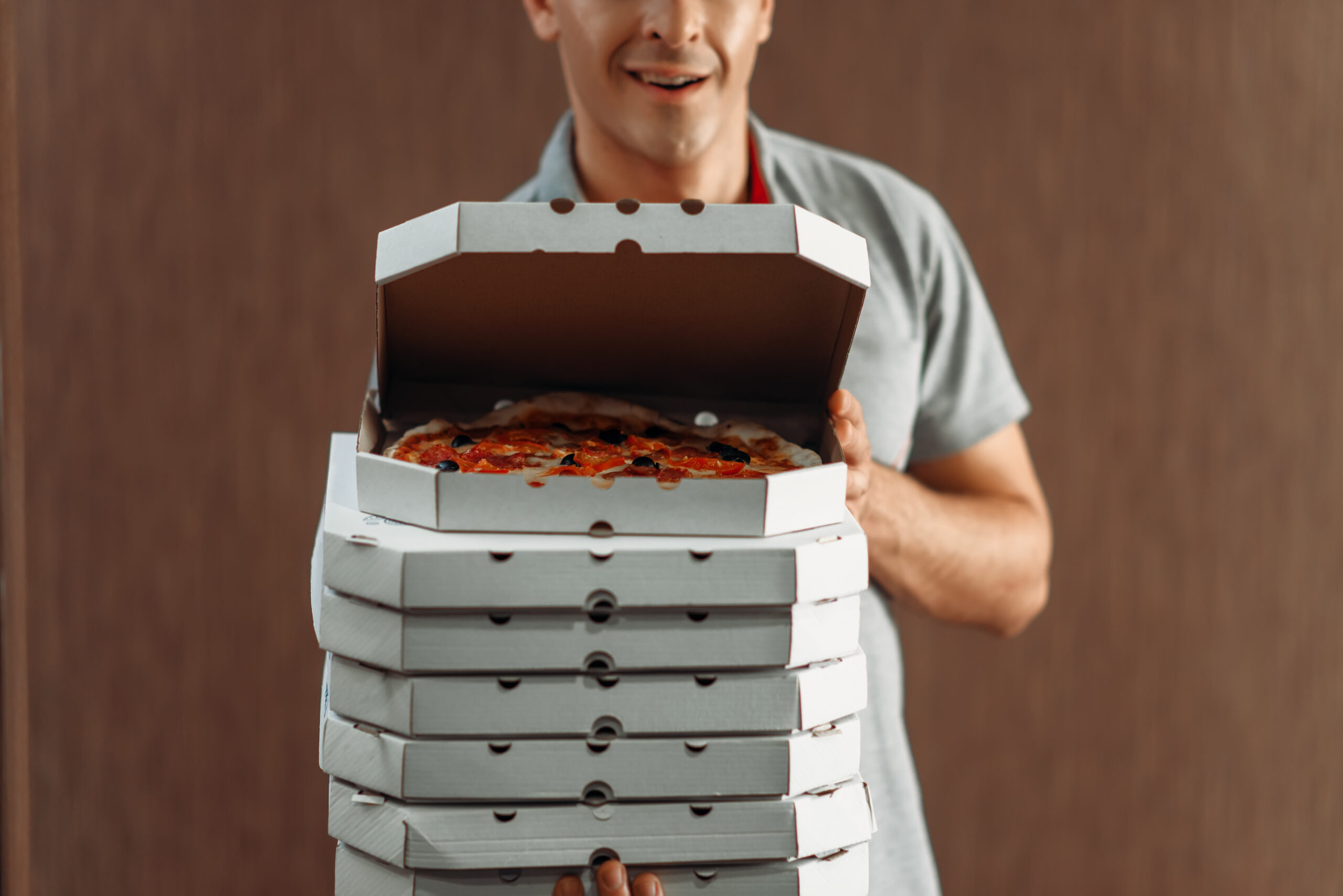 Ein Pizzabote hält mehrere Schachteln Pizza in den Händen. Die oberste Schachtel ist geöffnet und zeigt eine frische Pizza.