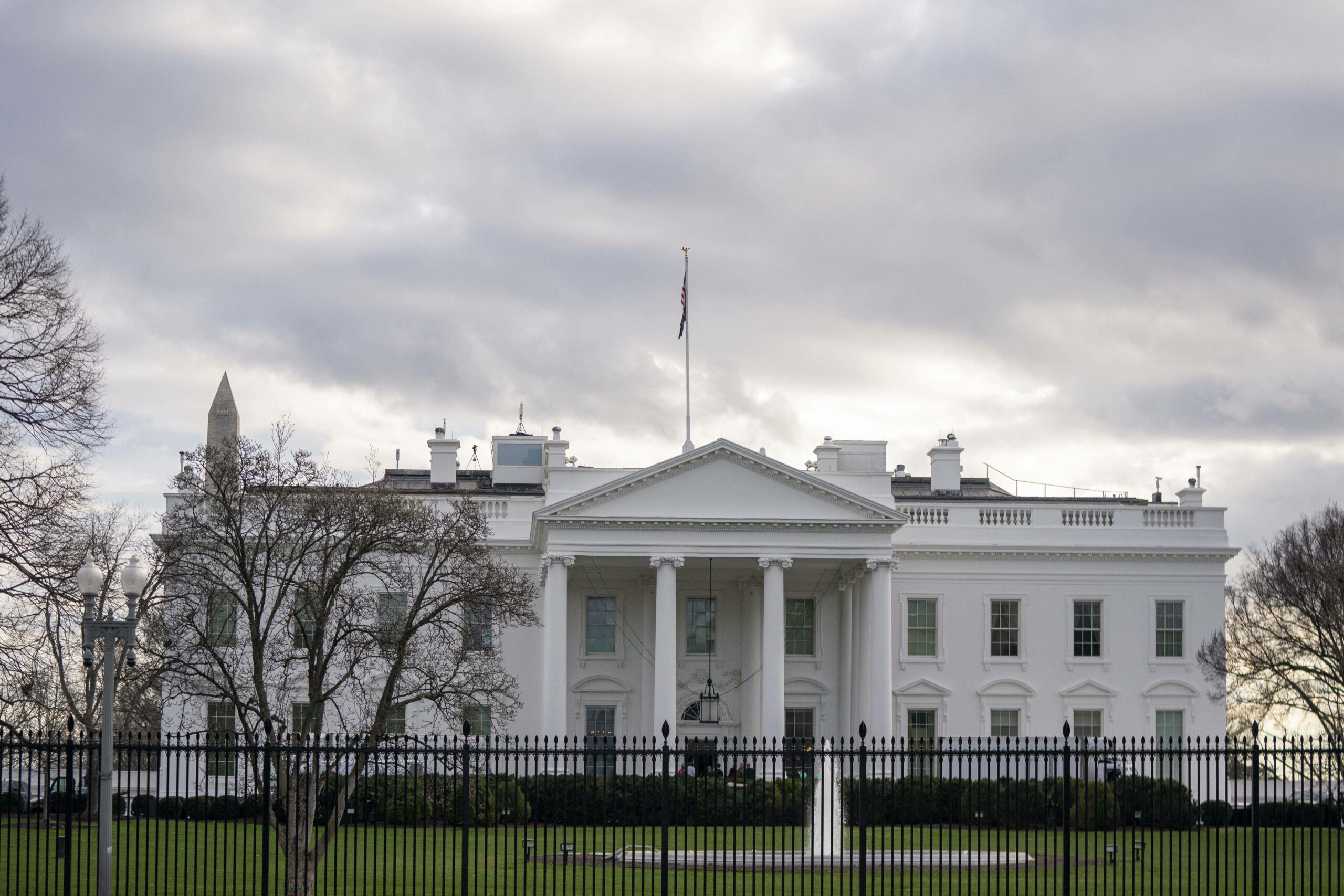 Das Weiße Haus in Washington, D.C. ist der Amtssitz des US-Präsidenten. Im Vordergrund steht ein Zaun. Der Himmel ist bewölkt. Die Bäume sind winterlich kahl. (Symbolbild)